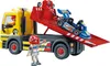 A yellow tow truck with a red trailer carrying a blue go-kart, with a Playmobil figure standing next to it. Produktbild-Vorschau