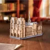 A wooden 3D model of the Notre Dame Cathedral sits on a wooden table, with a blurred background of bookshelves and curtains. Náhled obrázku produktu