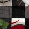 A close-up view of a rug with a checkered pattern and abstract red and gray curves. Parts of wooden chair legs and a white table are visible. Anteprima dell’immagine prodotto
