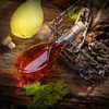 A bottle of amber liquid with a cork stopper sits on a wooden surface, surrounded by pine cones and moss. Another bottle with yellow liquid is in the background. Anteprima dell’immagine prodotto