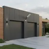 A modern garage with two large gray doors, illuminated by a solar-powered LED street light mounted on the wall above. Produktbild-Vorschau
