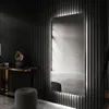 A modern hallway with a slatted black wall, a console table with a sculpture, a stool, and a large illuminated mirror. Produktbild-Vorschau