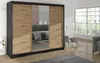 A modern sliding door wardrobe with black frames and oak artisan wood-effect doors, positioned in a well-lit room with a large window. Náhľad obrázku produktu
