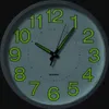 A close-up view of a white wall clock with green luminous numbers and hands. Voir les images du produit