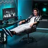 A young man is sitting in a gaming chair in a room with blue ambient lighting, playing a video game. Produktbild-Vorschau