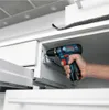 A person is using a cordless drill to screw something into a cabinet. Voir les images du produit
