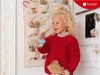 A young girl is holding a small blue fairy figurine in front of a fabric advent calendar with numbered pockets. Produktbild-Vorschau