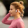 A woman wearing headphones and a pink long-sleeved shirt outdoors. Produktbild-Vorschau