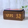A digital alarm clock with a wooden finish is shown on a table, with a smartphone placed on top. Produktbild-Vorschau