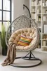 A hanging egg chair with a cushion and blanket is placed in a room with a bookshelf and a window. Produktbild-Vorschau