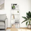 A white bookshelf filled with books and decorative items, next to a gray sofa and a large potted plant. Náhled obrázku produktu