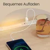 A smartphone is charging on a wooden surface next to a power strip with an integrated LED light and a glass of tea. Náhled obrázku produktu