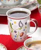 A close-up shot of a coffee mug filled with coffee, placed on a red placemat. Other tableware items are visible in the background. Náhľad obrázku produktu