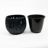 Two black planters are shown against a white background. The planter on the left has a decorative, wavy pattern with cutouts, while the planter on the right is a solid, smooth cylinder. Náhľad obrázku produktu
