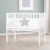 A white crib with a gray star pillow inside, set against a light blue wall and a wooden floor. Produktbild-Vorschau