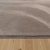 A close-up view of a fluffy, high-pile rug with a wavy pattern, resting on a wooden floor. Voir les images du produit