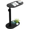 A black C-shaped side table with a cup of coffee and a magazine on top, and a plant and books on the lower shelf. Produktbild-Vorschau