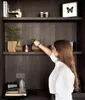 A woman is arranging plants on a shelf. Voir les images du produit