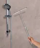 A hand holding a shower squeegee next to a shower head on a textured wall. Produktbild-Vorschau