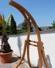 A wooden hammock stand is shown outdoors on a patio with a palm tree and houses in the background. Produktbild-Vorschau