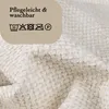 A close-up of a textured off-white fabric, with a beige rounded rectangle overlay containing care instructions and symbols. Produktbild-Vorschau