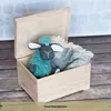 A wooden box with a lid open, containing a teal knitted sheep toy and a gray patterned blanket. Produktbild-Vorschau