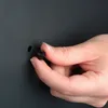 A hand is holding a small black object near a dark gray surface with a hole. Produktbild-Vorschau