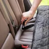 A hand is shown securing a black quilted car seat cover to a car's seatbelt buckle. Náhľad obrázku produktu