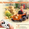 A child is riding an orange toy tractor with a trailer full of pumpkins, in a farm-like setting with hay bales and a house in the background. A remote control is held in the foreground. Náhľad obrázku produktu