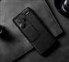 A black phone case with a carbon fiber texture is shown on a dark textured surface, possibly a desk or table. The case has a sliding cover for the camera module. Podgląd zdjęcia produktu