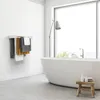 A modern bathroom with a freestanding bathtub and a large window overlooking greenery. A wall-mounted towel rack with several towels is visible on the left. Produktbild-Vorschau