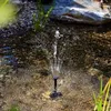 A solar-powered fountain spraying water in a shallow pond with rocks and plants. Produktbild-Vorschau