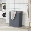 A dark gray laundry basket with a beige towel draped over it, placed in a laundry room with washing machines and tiled walls. Náhled obrázku produktu