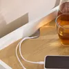 A close-up view of a bedside table with a charging cable and a glass of amber liquid. Produktbild-Vorschau