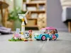 A LEGO set featuring a wind turbine, solar panels, a car, and two mini-doll figures, set up on a wooden floor with a blurred background of a room. Náhled obrázku produktu