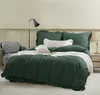 A neatly made bed with green bedding, pillows, and a throw blanket, in a room with a chair and a lamp. Podgląd zdjęcia produktu