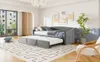 A grey daybed with a trundle bed pulled out, set up in a bright, modern living room with large windows and artwork on the wall. Produktbild-Vorschau