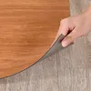 A hand is peeling up a section of self-adhesive wood-effect flooring, revealing the adhesive backing and the underlying floor. Anteprima dell’immagine prodotto