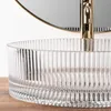 A close-up of a transparent glass sink with a gold faucet and a mirror in the background, resting on a wooden surface. Anteprima dell’immagine prodotto