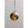 A decorative glass ball ornament with LED lights inside, hanging against a brick wall. Podgląd zdjęcia produktu