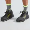 A close-up shot of a person's feet wearing black and yellow U-Power safety sneakers and grey socks with yellow accents. Produktbild-Vorschau