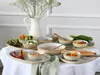A table setting with a variety of ceramic dishes filled with food and a pitcher of flowers. Produktbild-Vorschau