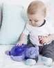 A baby is sitting on a bed and playing with a purple stuffed turtle toy. Voir les images du produit