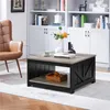 A square coffee table with a shelf is placed on a rug in a living room setting, with a chair and bookshelves in the background. Produktbild-Vorschau