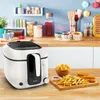 A white Tefal deep fryer is shown on a wooden countertop, with a bowl of fried onion rings and a platter of french fries and fish sticks in front of it. The background shows a kitchen shelf with various items. Produktbild-Vorschau
