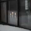 Three lit candles are visible through a window with snow on the sill. Produktbild-Vorschau