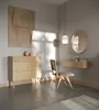 A minimalist bedroom or dressing area with a wooden dresser, chair, and floating shelf. Produktbild-Vorschau