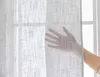 A hand is shown touching a sheer gray curtain in front of a window. Produktbild-Vorschau