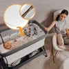 A woman sitting in a chair next to a baby bassinet where a baby is sleeping. The bassinet has stuffed animals inside. Produktbild-Vorschau