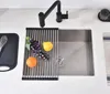 A kitchen sink area with a black faucet, a roll-up drying rack with fruit, and a cutting board. Náhled obrázku produktu